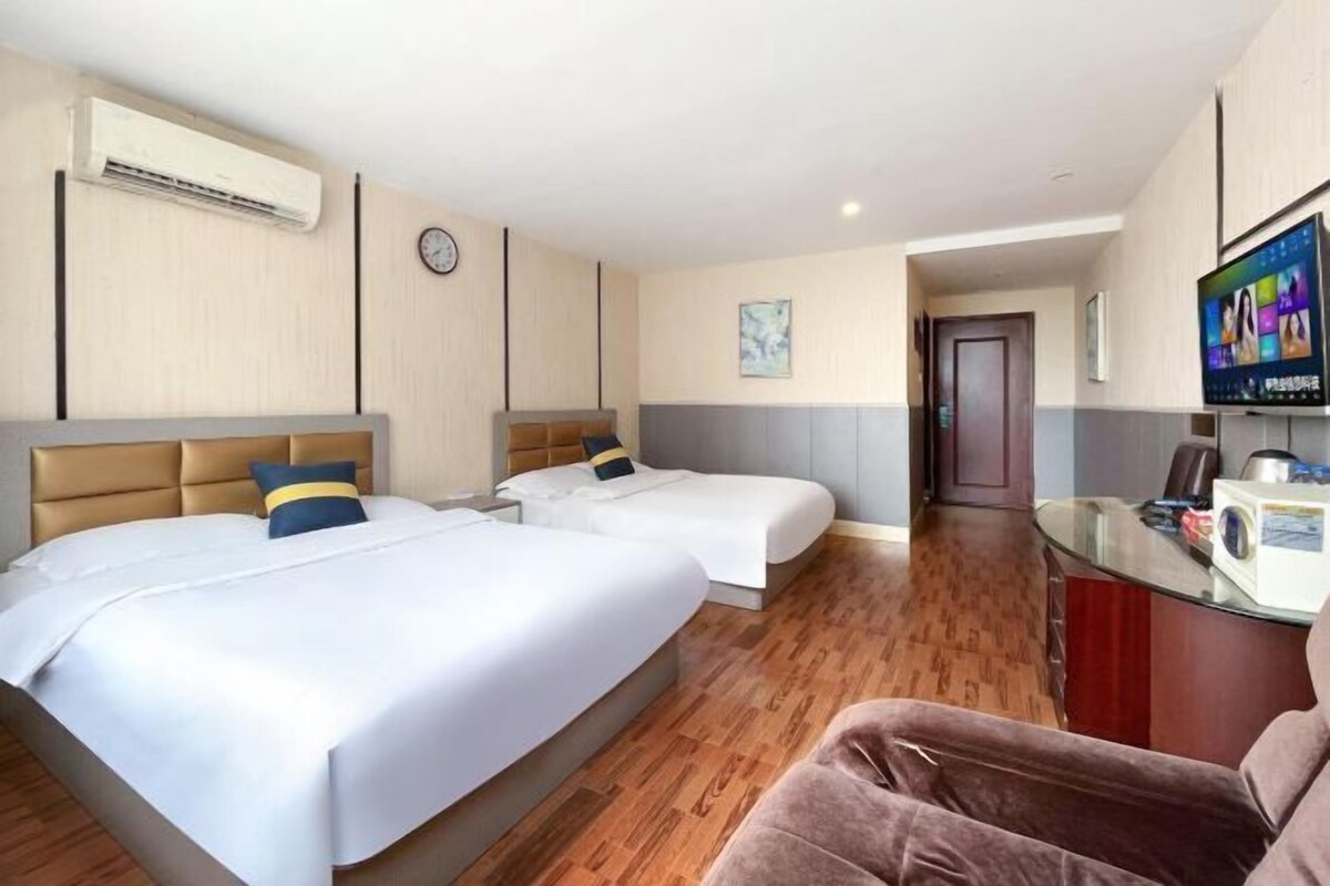 Una habitación de hotel con dos camas, televisión, escritorio y un reloj en la pared.