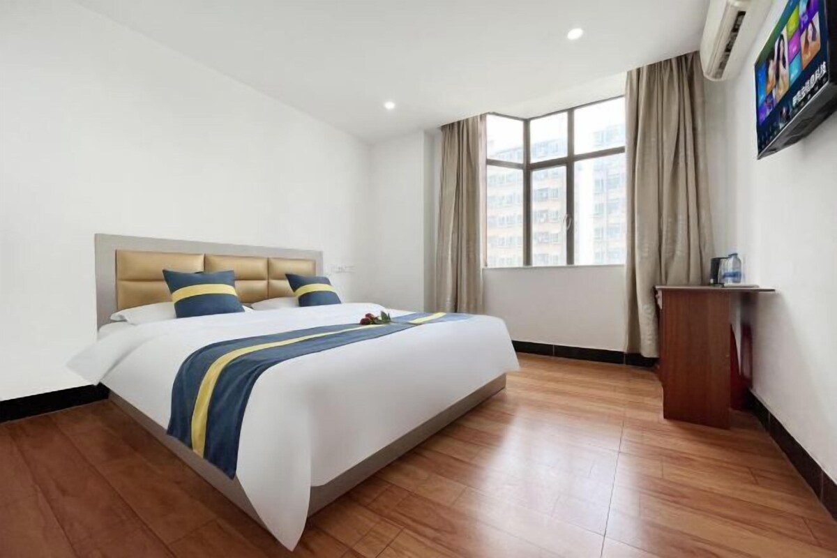 Habitación de hotel con una cama grande, piso de madera, ventana con cortinas y televisor en la pared.