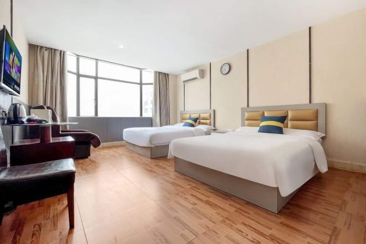 A hotel room with two beds, a desk, a chair, a TV, and a large window.