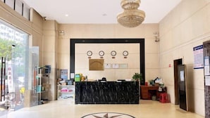 A hotel reception area with a marble counter, a chandelier, and a large circular floor design. - Kaerlaisi Boutique Stay (Dongguan Chang'an) (Dongguan)