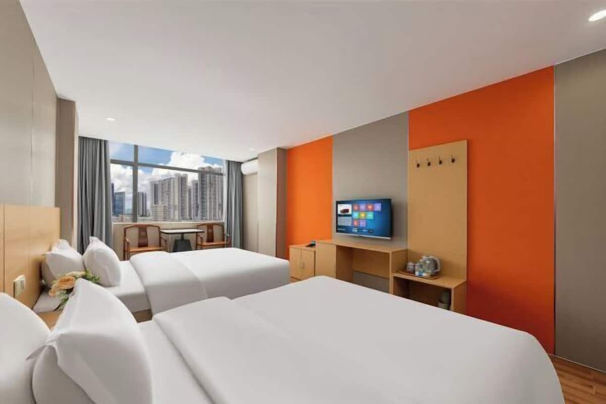 A hotel room with two beds, a desk, a television, and a city view.