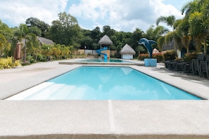 A swimming pool with a slide, surrounded by tropical vegetation and thatched-roof huts. - Reddoorz @ Afamosa Villas Resort Ilocos Sur (San Juan)