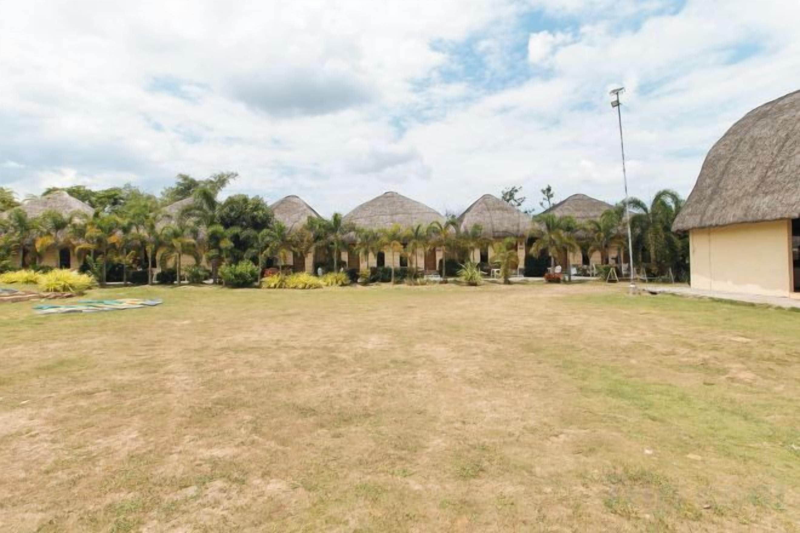 A series of thatched-roof structures with a grassy lawn in front.