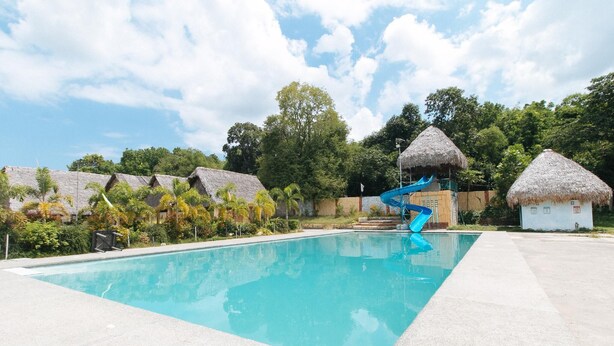A swimming pool with a blue slide, thatched-roof huts, and lush greenery. - Reddoorz @ Afamosa Villas Resort Ilocos Sur (San Juan)
