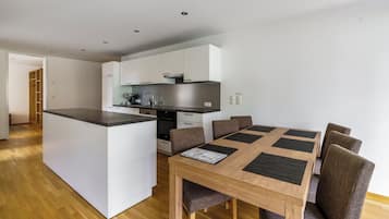 Una cocina moderna con armarios blancos, una isla central y un comedor con mesa y sillas de madera.
