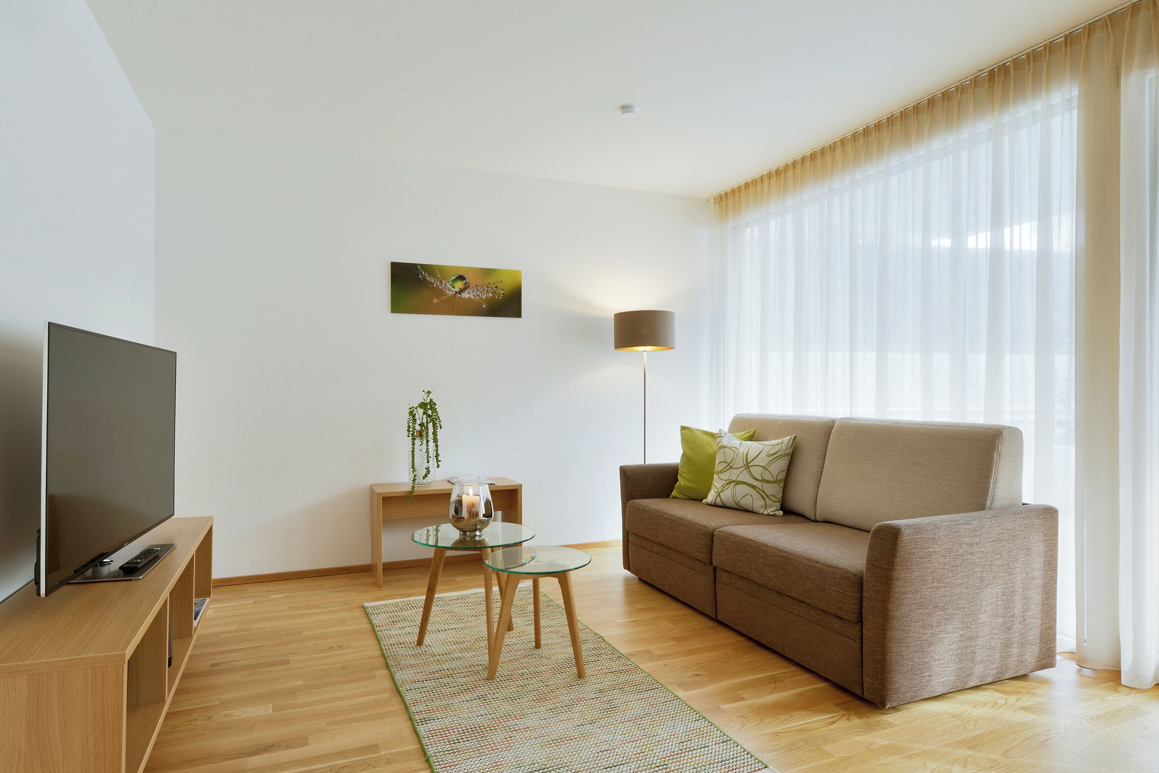 Una sala moderna con un televisor de pantalla plana, un sofá, una mesa de centro de vidrio y una lámpara.