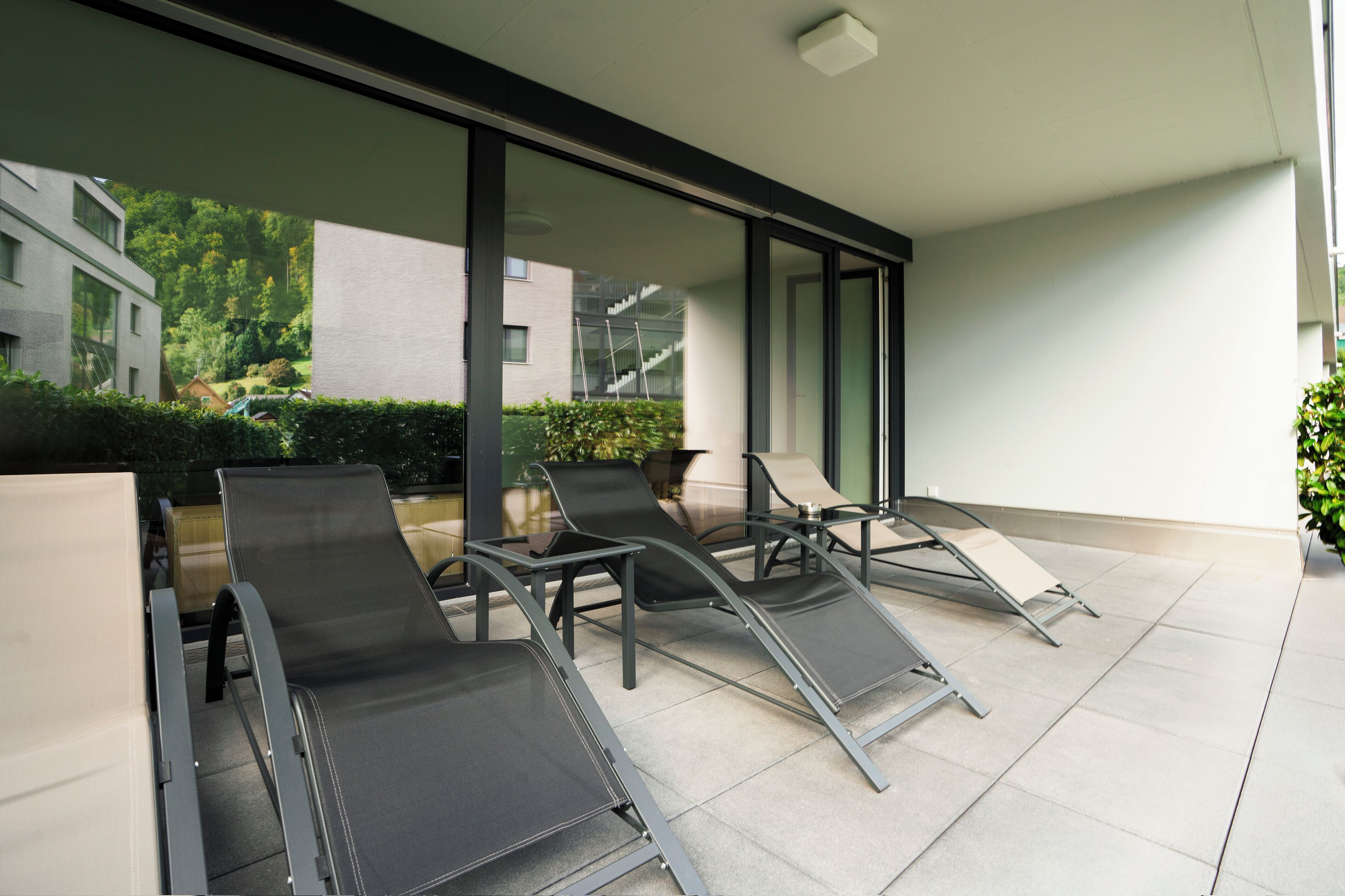 Un área de estar exterior moderna con sillas de metal y una partición de vidrio.