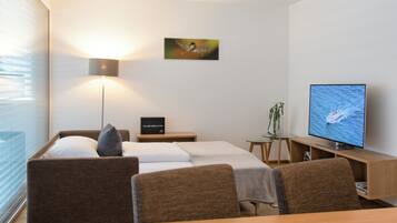 A modern hotel room with a bed, a desk, a television, a lamp, and a small plant.