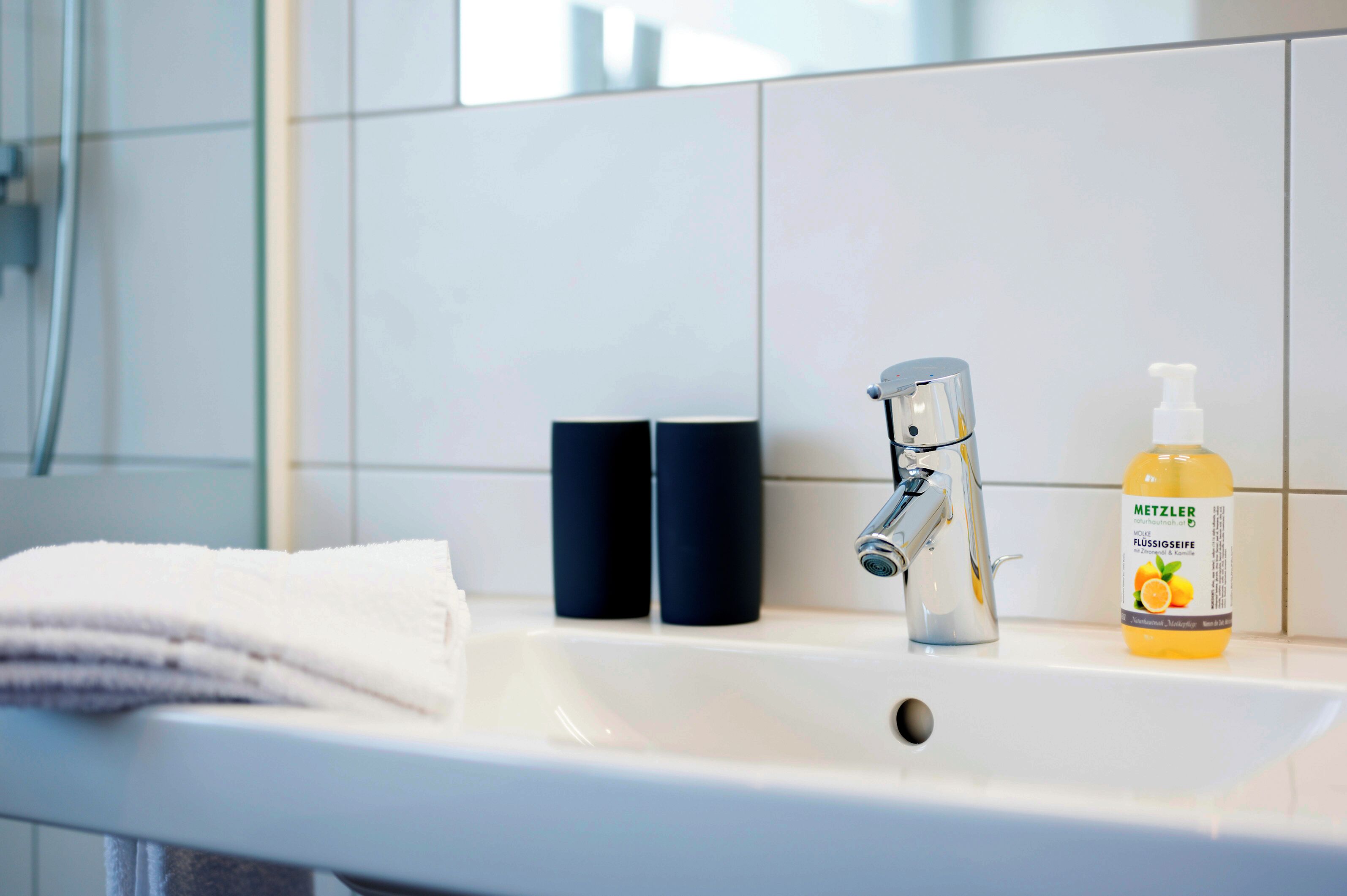Un lavabo de salle de bain avec une serviette blanche, deux distributeurs de savon noirs et un flacon de savon pour les mains de la marque Metzler.