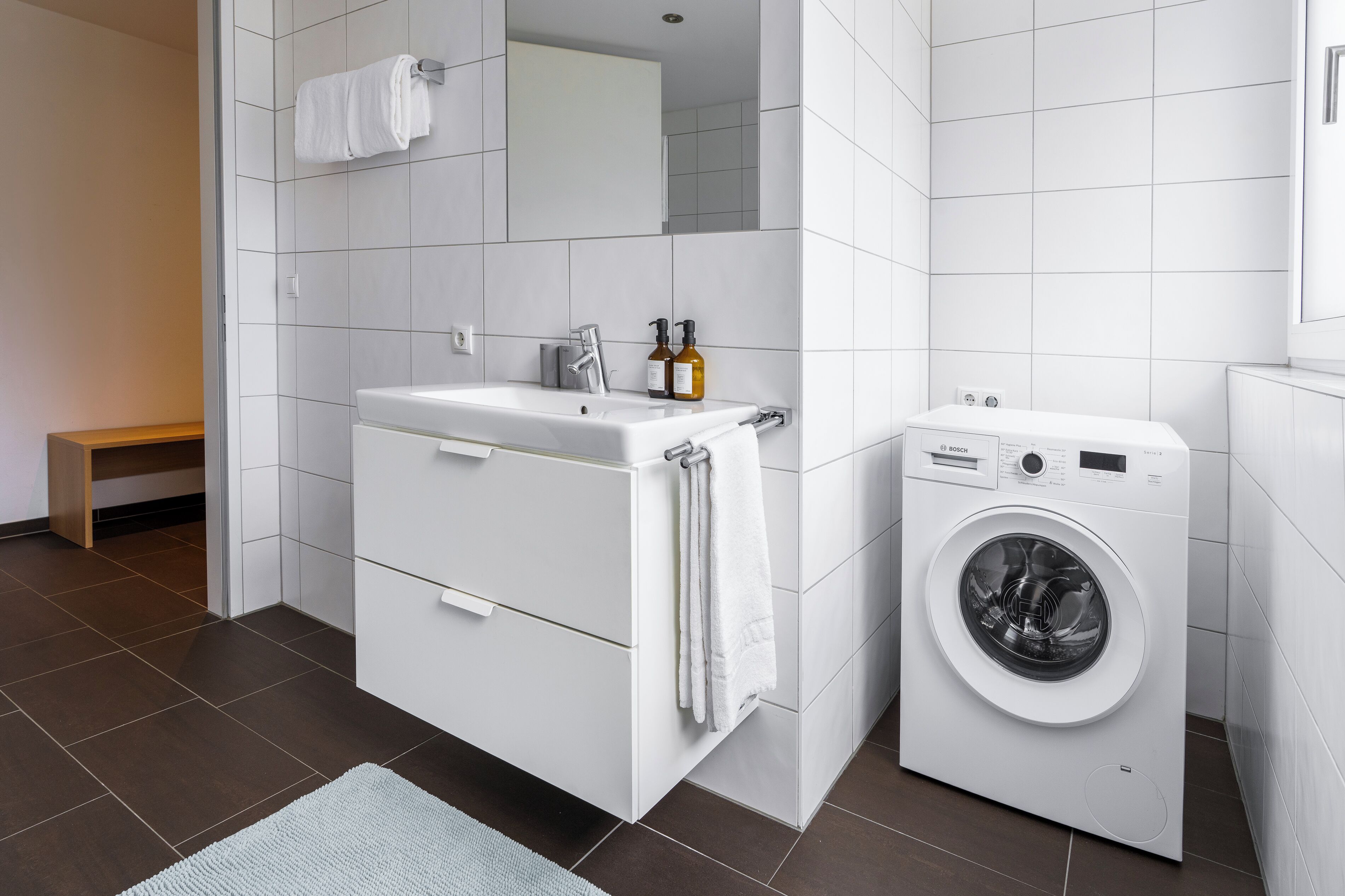 A modern bathroom with a white sink, mirror, and a front-loading washing machine.