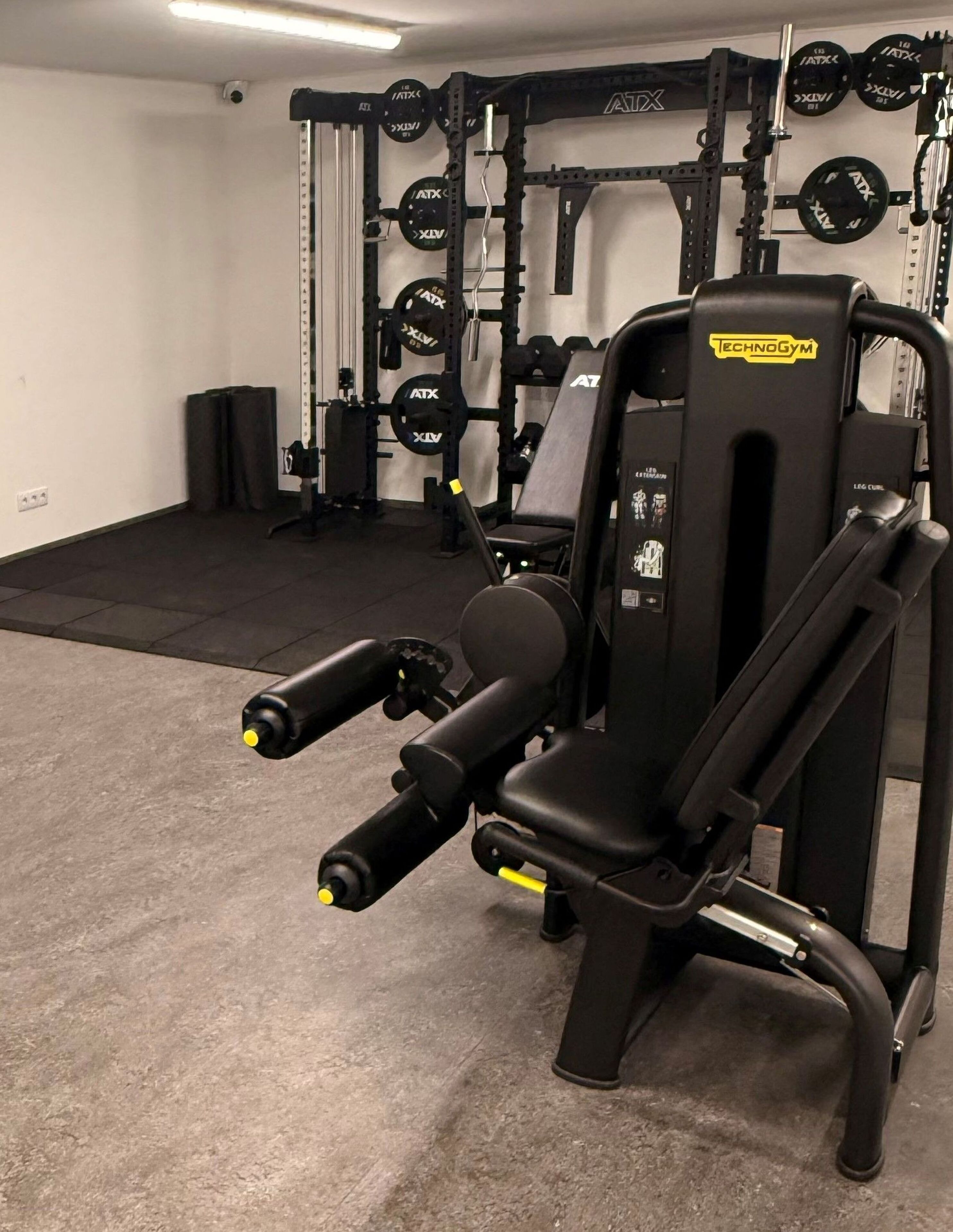 Un gimnasio con banco de pesas, jaula para sentadillas y diferentes discos de pesas.