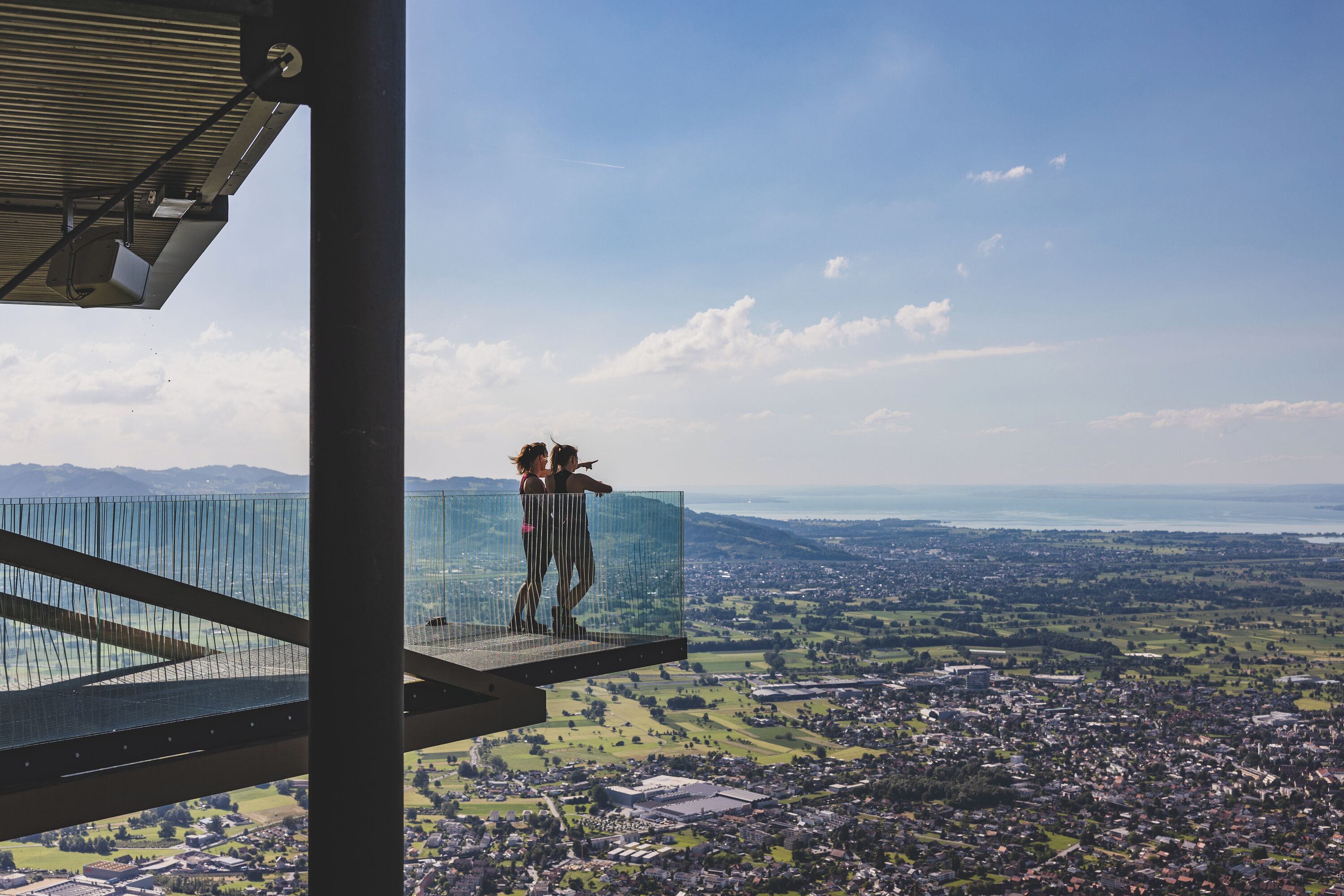 Uma ponte de vidro com vista para uma cidade e montanhas ao fundo.