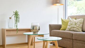 A modern living room with a glass coffee table, a glass wine glass, a hanging plant, a lamp, and a sofa with cushions.
