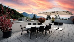Terraza en la azotea con mesa, sillas, una sombrilla grande y plantas en macetas.