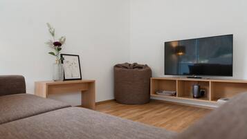 A modern living room with a flat-screen TV, a brown bean bag, a small table with a vase and picture frame, and a sofa.