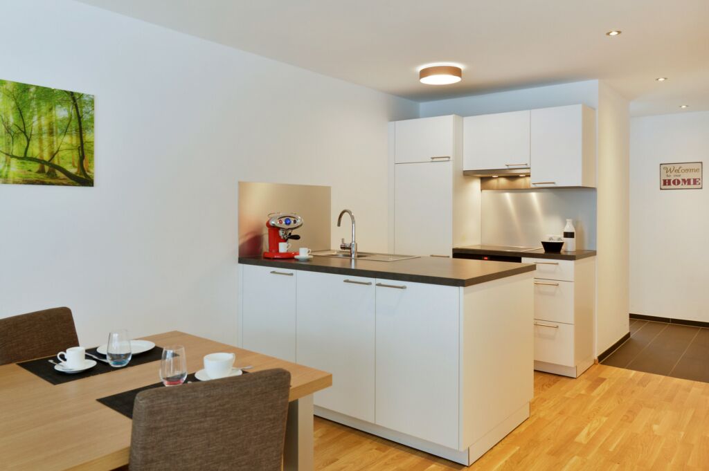 Een moderne keuken met witte kastjes, een centraal eiland en een eethoek met een tafel en stoelen.
