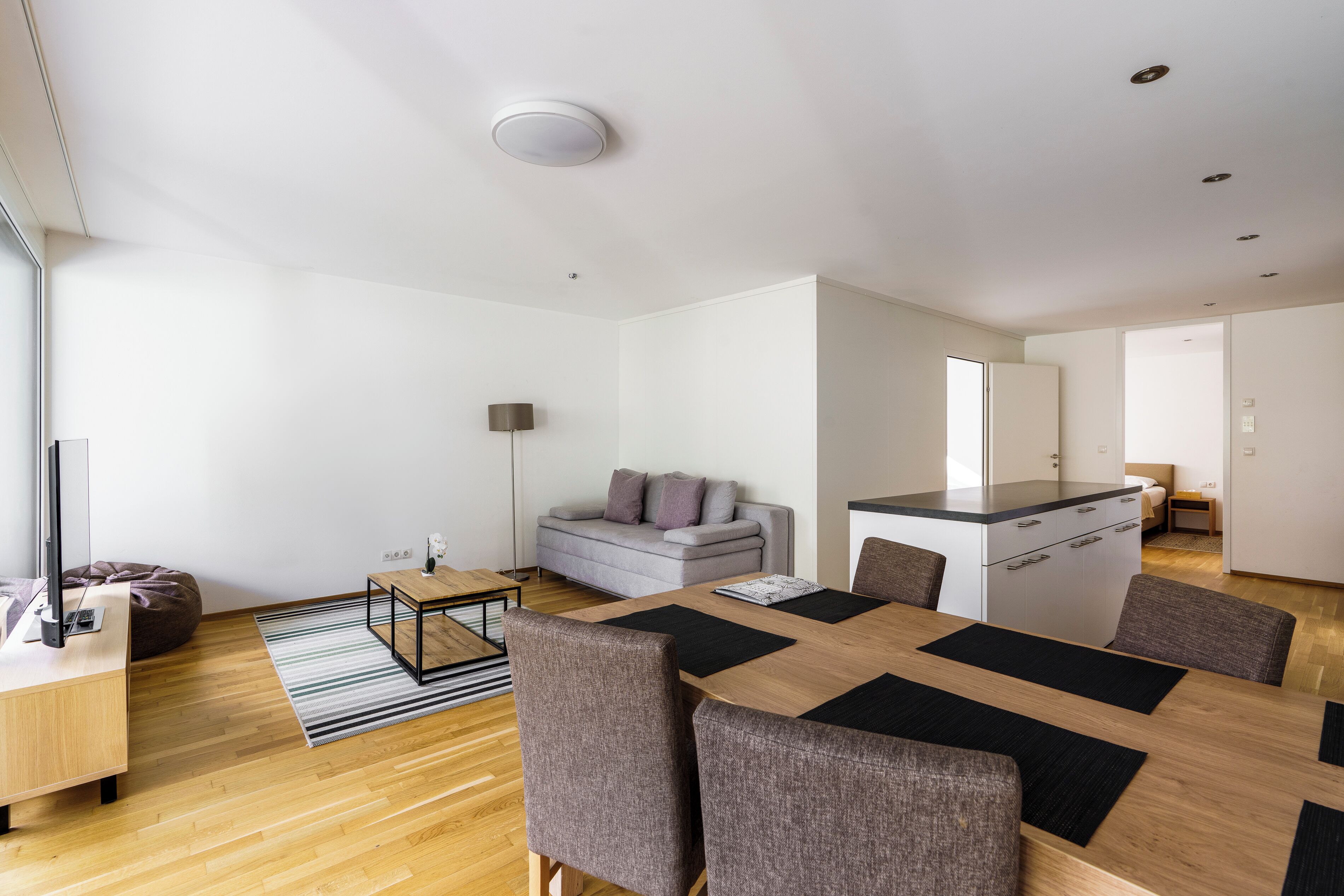 A modern living room with a sofa, a coffee table, and a dining area with a table and chairs.
