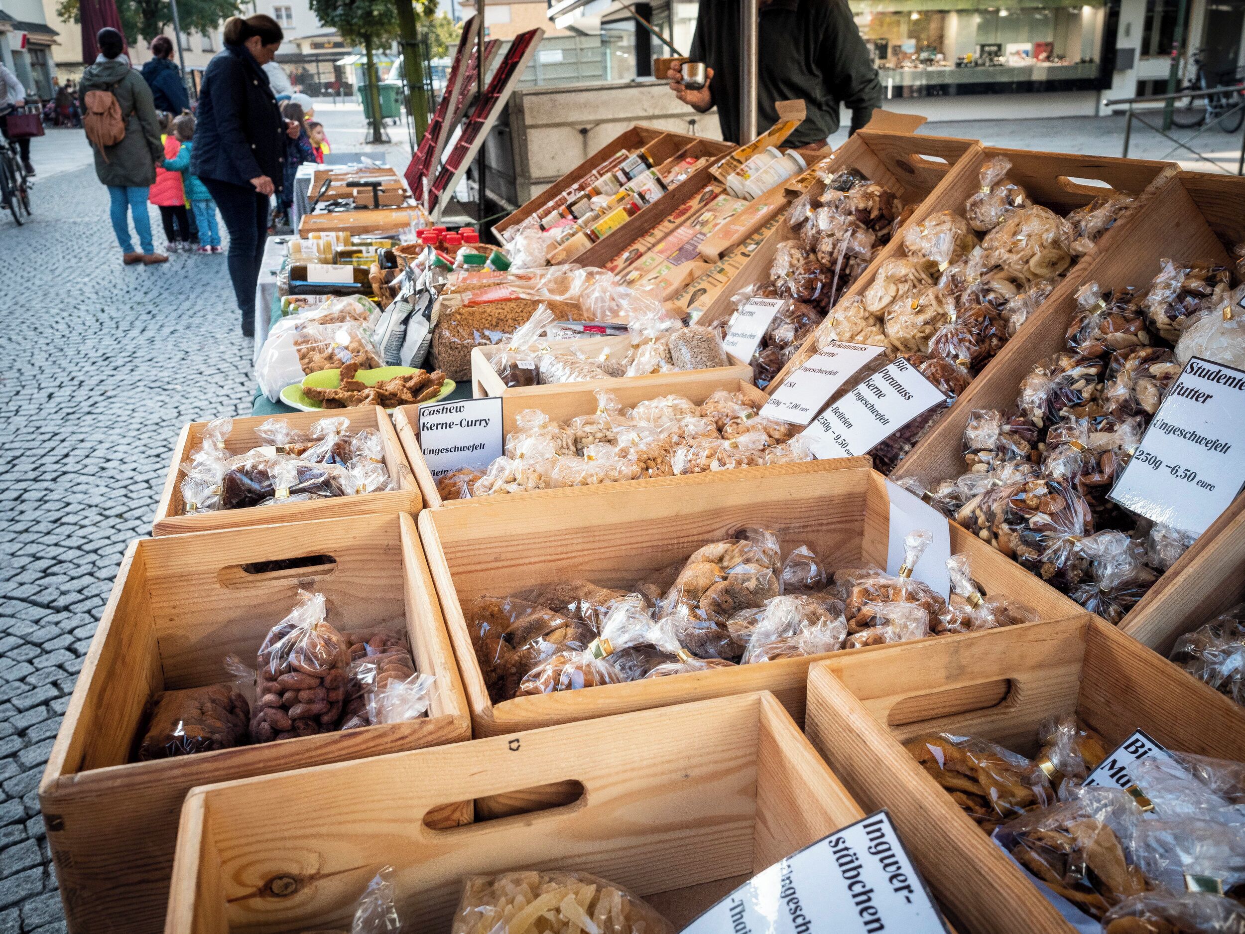 A market stall with various food items displayed in wooden crates, including dried fruits and nuts.