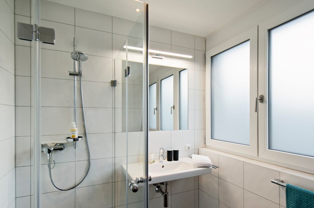 Un baño moderno con cabina de ducha de vidrio, un lavabo blanco y un espejo grande.