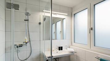 Un baño moderno con cabina de ducha de vidrio, un lavabo blanco y un espejo grande.