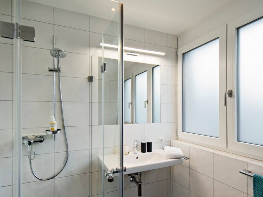 Un baño moderno con cabina de ducha de vidrio, un lavabo blanco y un espejo grande.