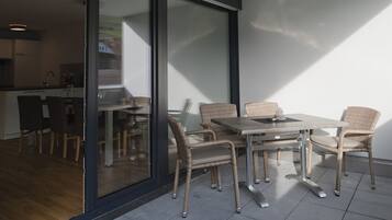 Un área de comedor exterior moderna con sillas de mimbre y una mesa de metal, contigua a un piso corredizo que da a una cocina.