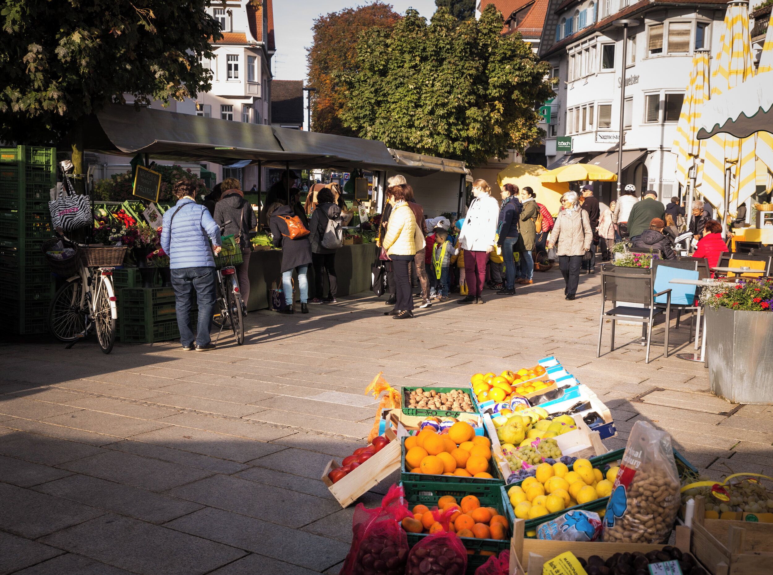 Ein lebhafter Markt im Freien mit verschiedenen Ständen, auf denen Obst und Gemüse verkauft werden.