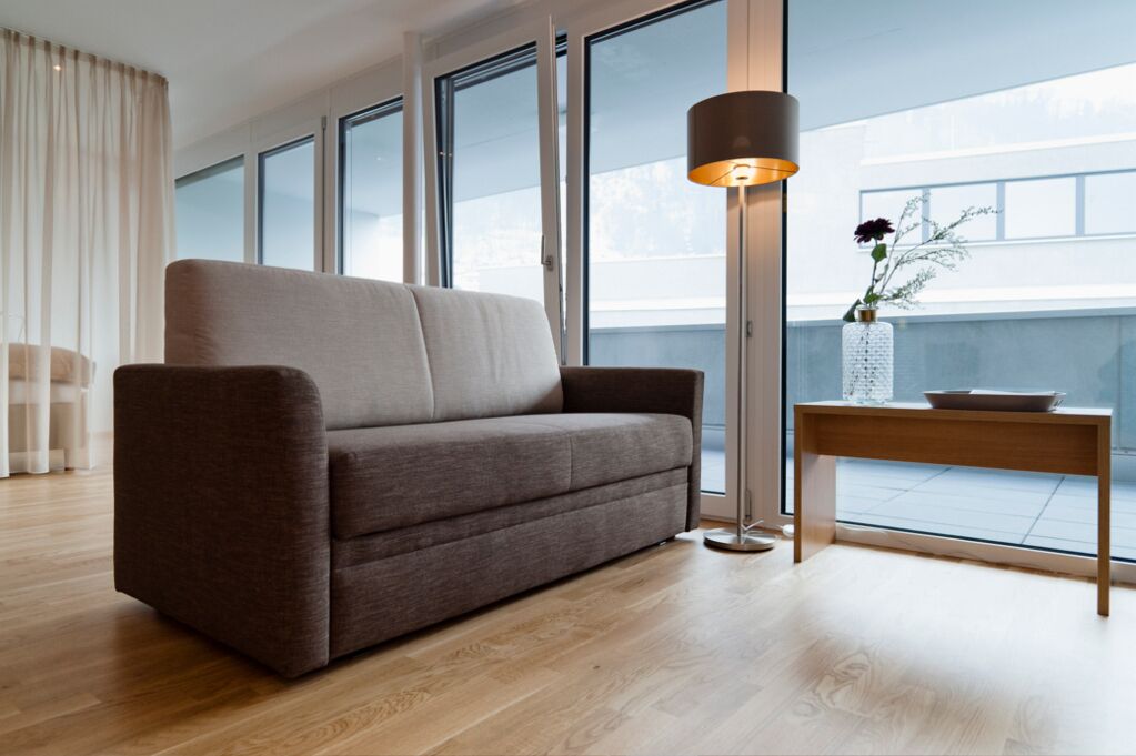 A modern living room with a sofa, a table with a vase, and large windows.