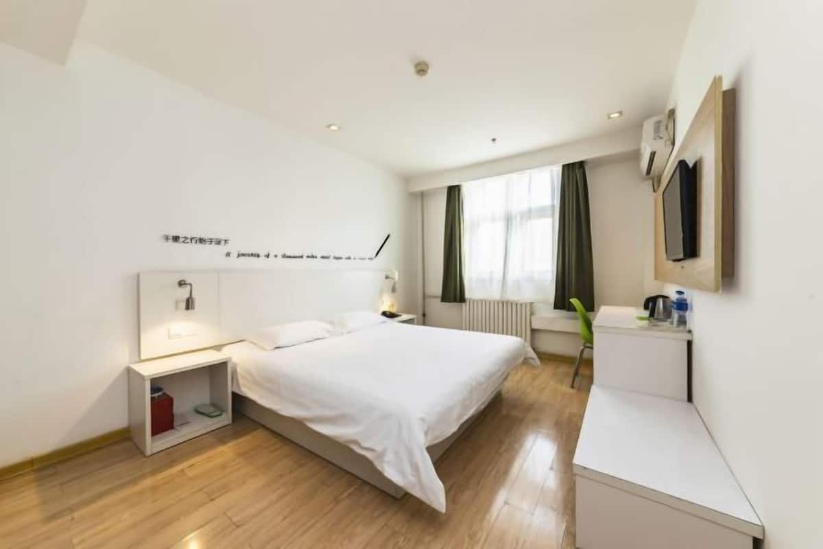 A modern hotel room with a large bed, bedside table, and a small desk area.