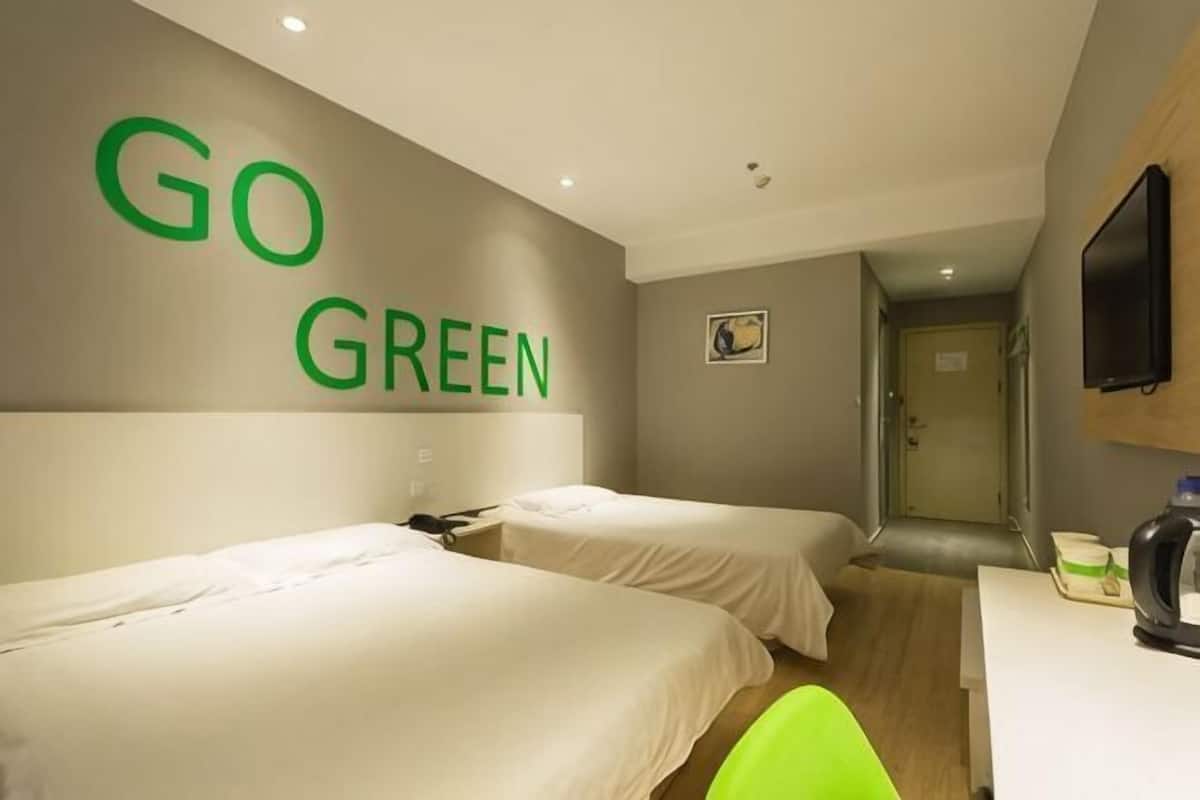 A hotel room with two beds, a desk, a television, and a 'GO GREEN' sign on the wall.