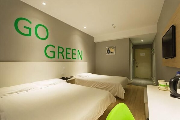 A hotel room with two beds, a desk, a television, and a 'GO GREEN' sign on the wall.