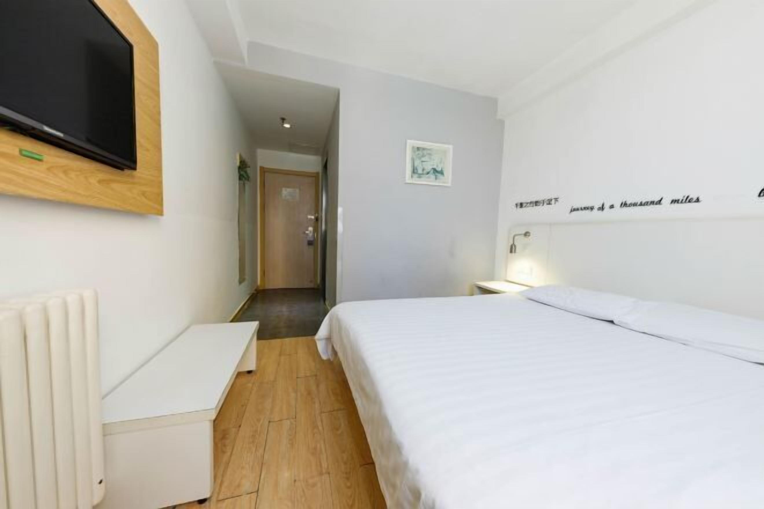 Ein Hotelzimmer mit Bett, Schreibtisch, Wandfernseher und einem zur angrenzenden Kammer führenden Flur.
