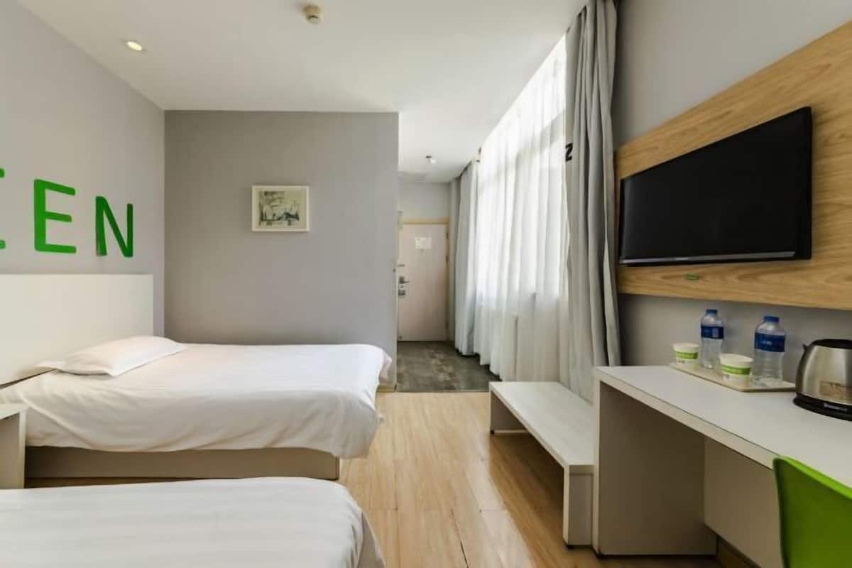 A hotel room with two beds, a desk, a television, and a window with curtains.