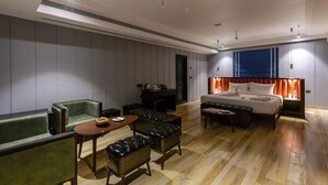 Une chambre d’hôtel moderne dotée d’un grand lit, d’un coin salon avec un canapé et des fauteuils, d’une petite table et d’une cheminée.