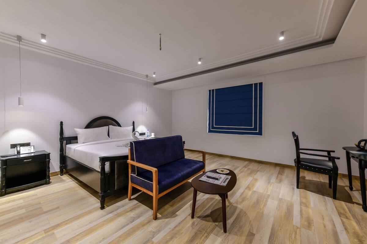 A hotel room with a bed, a blue sofa, a small table, a chair, and a nightstand.