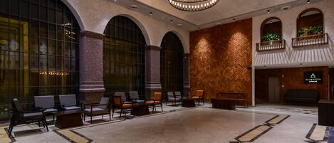 A spacious lobby with a large seating area, a decorative ceiling light, and a herringbone-patterned wall.