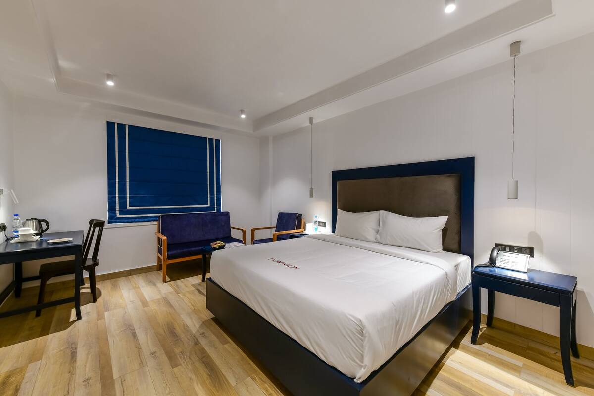 A hotel room with a large bed, a desk with a chair, a small table, and a blue accent wall.