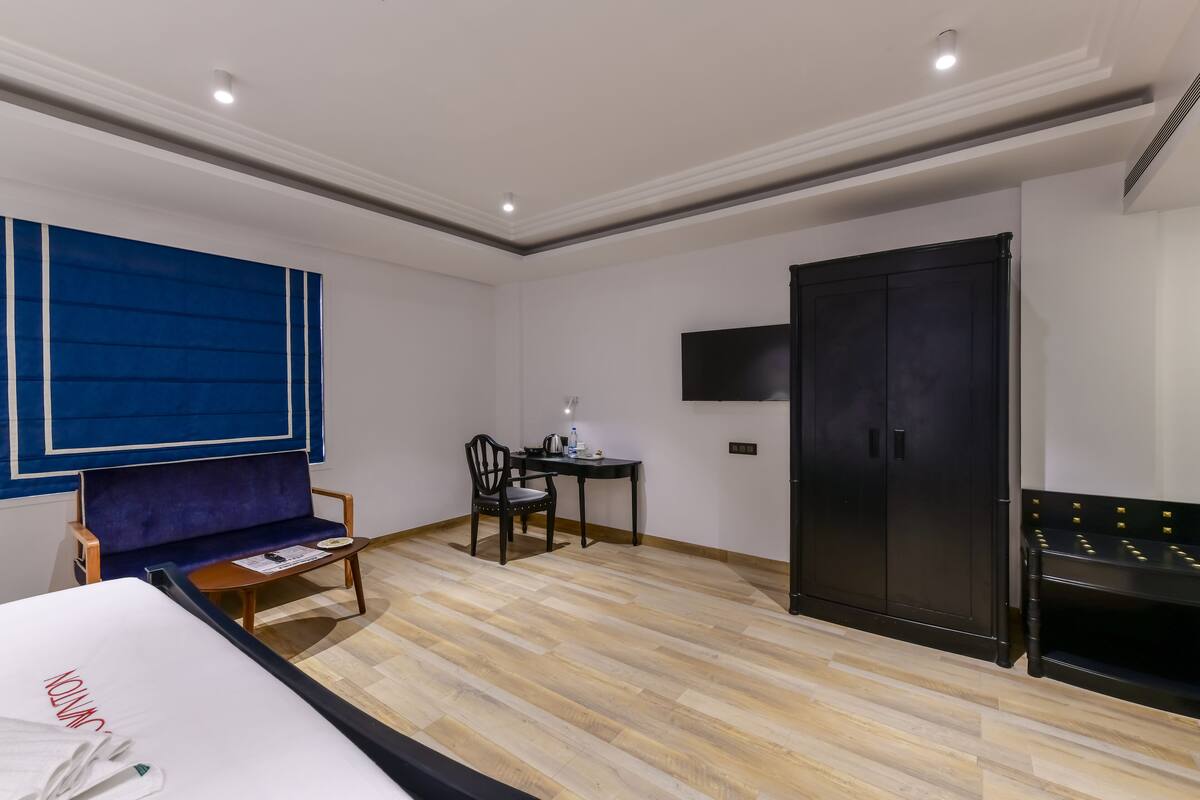 A hotel room with a bed, a desk with a chair, a TV, and a wardrobe.