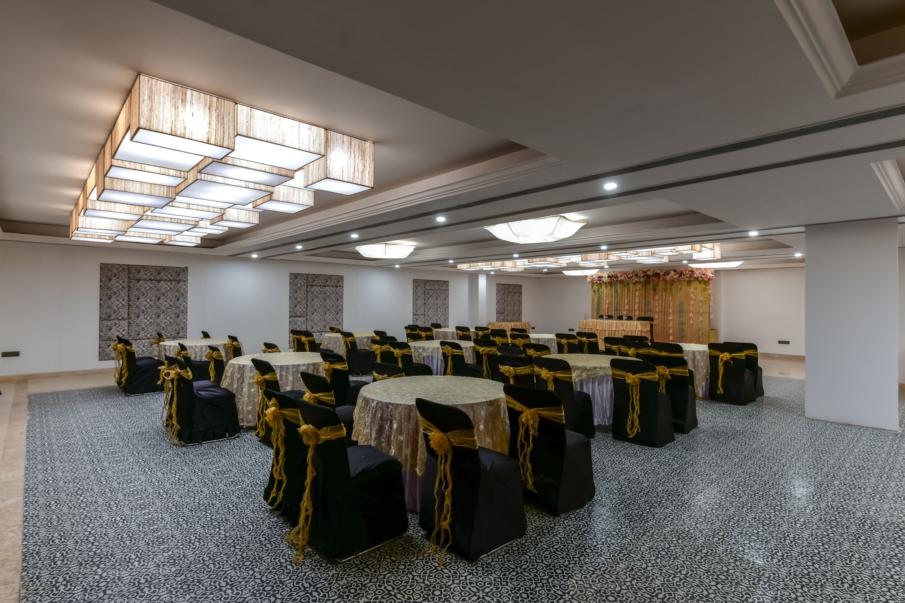 A large conference room with round tables and black chairs, decorated with gold sashes.