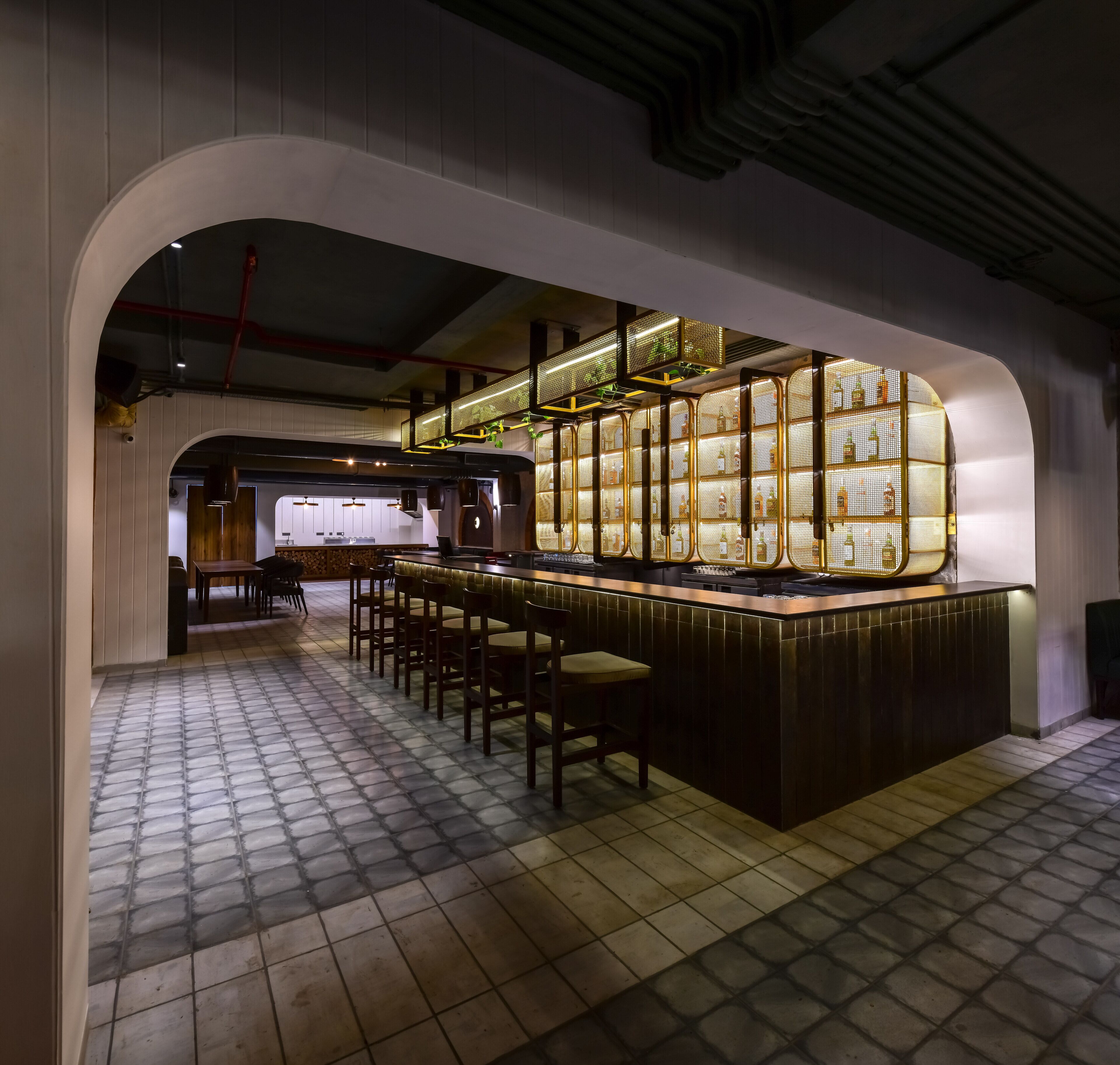 Zona de bar con piso de baldosas, barra de madera y varios taburetes.