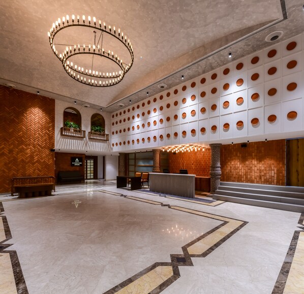 Um hall amplo com piso de mármore, um lustre circular e um balcão de recepção.
