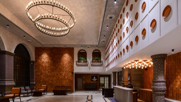 Un hall d’entrée spacieux avec un plafond haut, un lustre central et un comptoir de réception.