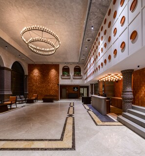 Um hall amplo com teto alto, um lustre central e um balcão de recepção.