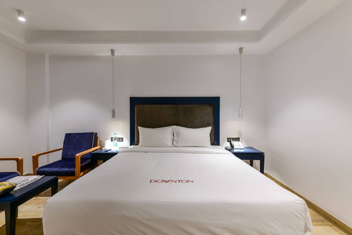 A hotel room with a large bed, a headboard, a desk with a chair, and a nightstand.