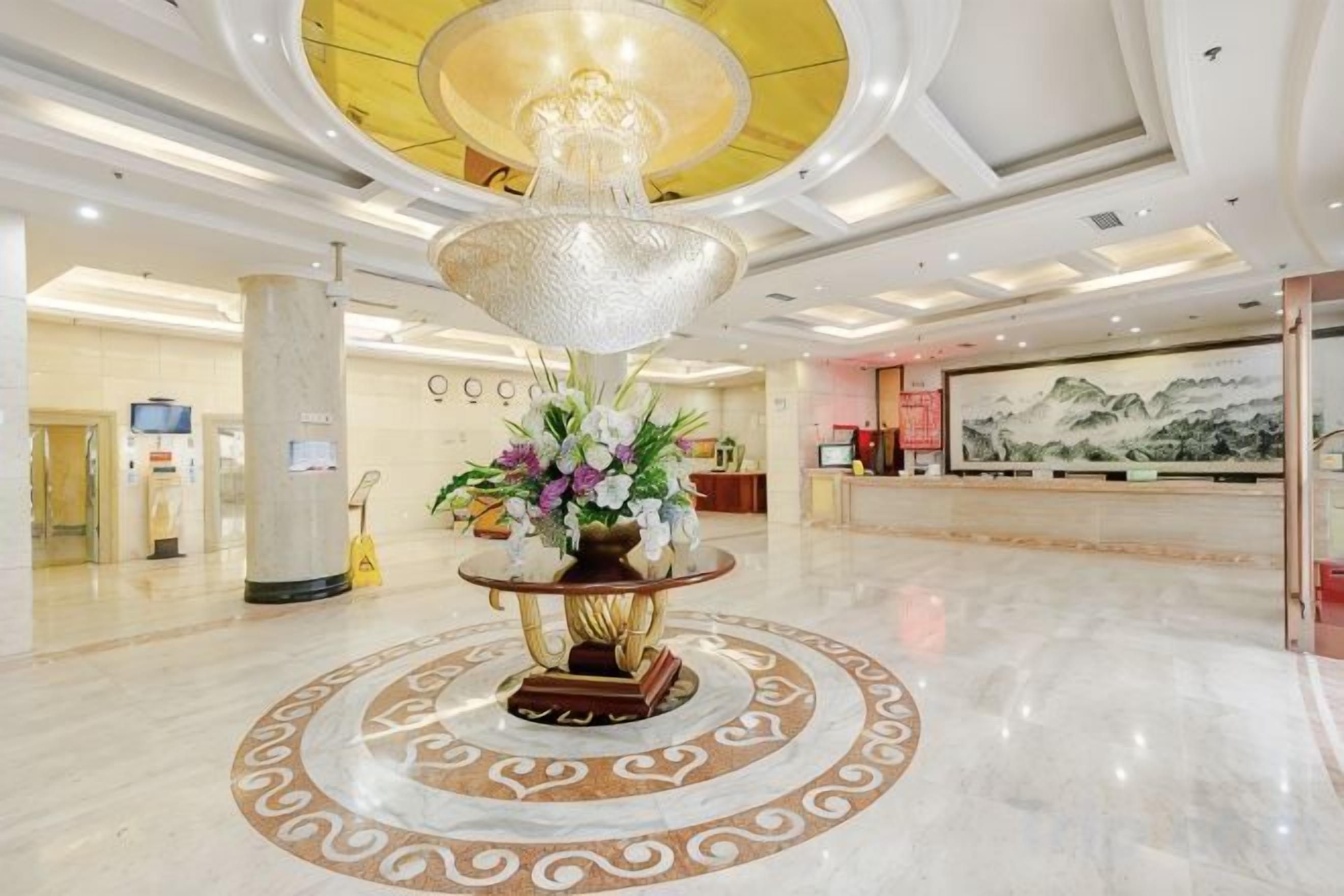 A lobby with a central decorative fountain, a reception desk, and a large mural on the wall.