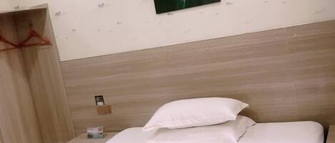 A hotel room with a wooden headboard, a bed with white linens, a small bedside table with a lamp, and a wall-mounted photo.