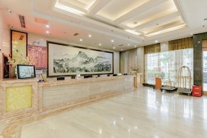 Zona de recepción de hotel con mostrador de mármol, una obra de arte enmarcada y un diseño de techo moderno.