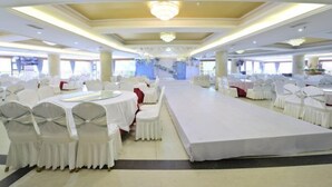 A banquet hall with round tables and white chairs, a stage, and a chandelier. - Fulong Hotel (Ya'an)