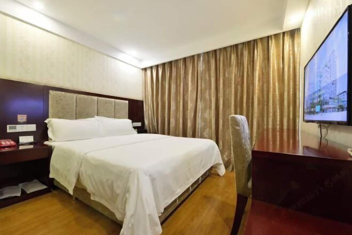 A hotel room with a bed, a desk, a chair, a television, and a curtain.