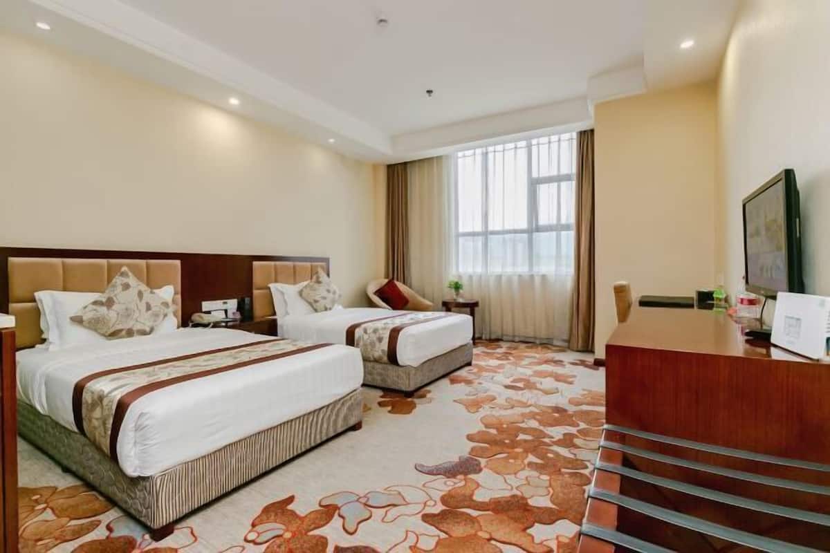 A hotel room with two beds, a desk, a chair, a TV, and a large window with curtains.